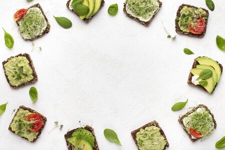 Vegan breakfast menu. Border of rye bread sandwiches with tofu, avocado and microgreen, top view,...
