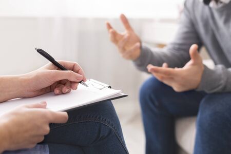 Psychotherapist writing notes, giving diagnosis to emotional man patient at counseling session, free spaceの写真素材