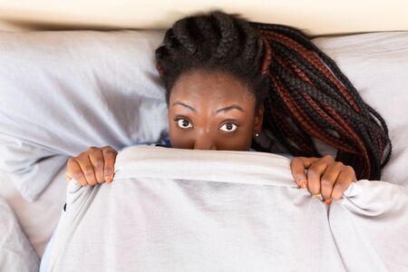 Good Morning. Playful Afro Girl Peeking Out Of Blanket Lying In Bed At Home. Top View