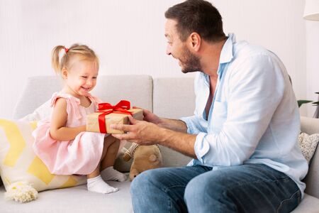 Happy Birthday. Excited dad congratulating his little daughter with present at homeの写真素材