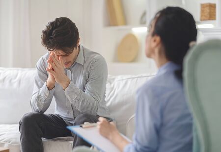 Troubled man feeling down at session with psychotherapist, experiencing difficult period in his lifeの写真素材