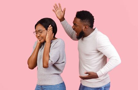 Domestic violence. Young african american man shouting at his girlfriend, woman covering ears with hands, pink studio backgroundの写真素材