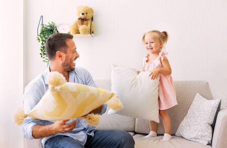 Family Morning Concept. Playful dad and daughter having a pillow fight together in the bedroomの写真素材