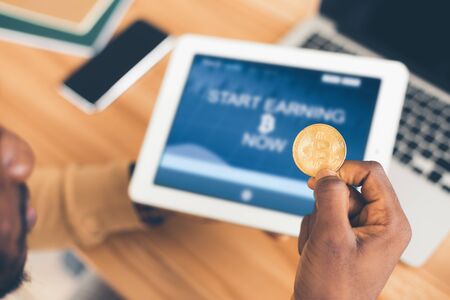 High Income. Black businessman earning money, holding bitcoin and tablet. Selective focus