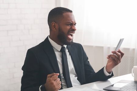 Enraged african american general manager reading on phone emails from displeased clients, angry with his employees, free spaceの写真素材