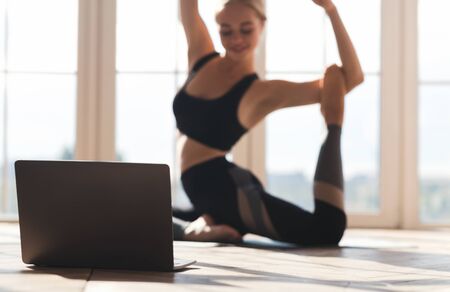 Sport, fitness application. Yoga girl exercising in front of laptop at home, selective focus, copy spaceの写真素材