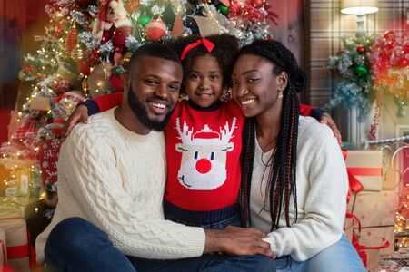 Christmas time. Portrait of cheerful black family of three celebrating winter holidays at home...