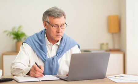No Ageism. Elderly Businessman Using Laptop And Taking Notes Working Sitting In Modern Office....