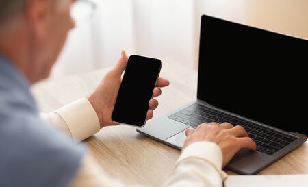 Unrecognizable Senior Man Using Phone And Laptop With Empty Screen Sitting At Workplace. Selective...