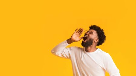 Stunned african american man in glasses screaming with excitement, keeping hand near mouth, yelling wow or omg, orange background, panorama with copy spaceの写真素材