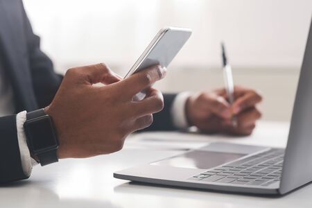 Black businessman using smartphone and taking notes, working in office, close up
