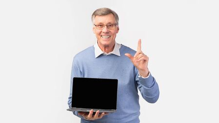 Great Offer. Smiling Senior Man Showing Laptop Blank Screen Pointing Finger Up Standing On White...