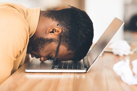 Desperate Employee. Depressed afro manager in eyewear resting head down on laptop keyboardの写真素材