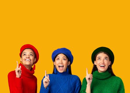 Look There. Three Smiling Diverse Girls Pointing Fingers Up At Copy Space Standing On Yellow Background. Studio Shotの写真素材