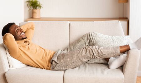 Lazy Weekend. Carefree African American Guy Lying Holding Hands Behind Head Relaxing On Sofa At Home.の写真素材