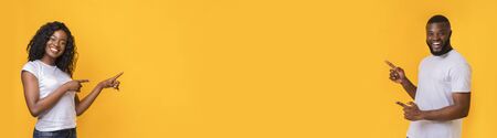 Awesome offer. Millennial african american couple pointing at empty space yellow background,...