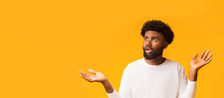 Amazed african american guy with raised hands and open mouth looking at copy space, seeing shocking...