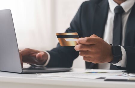 Cropped photo of african businessman making online transactions, using laptop and credit card