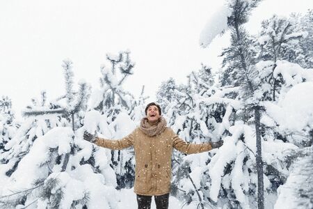 Cheerful Man Enjoying Winter Snowfall Standing Spreading Hands In Beautiful Snowy Forest. Christmas...