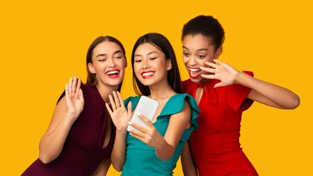 Hey. Three Party Girls Making Selfie On Smartphone Waving Hands Having Fun Over Yellow Background In...