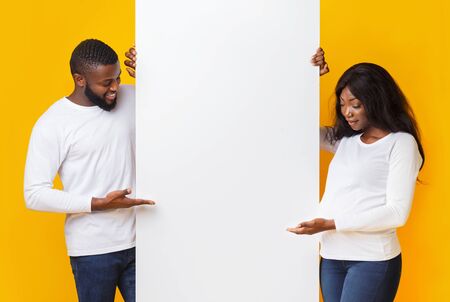 Pregnant african couple demonstrating blank advertising board over yellow studio background, mockupの写真素材