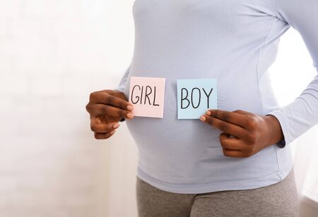 Cropped photo of pregnant black lady holding pink and blue cards next to belly, guessing gender of...