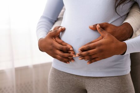 African man and woman hands over pregnant lady belly, family concept, close up, empty space