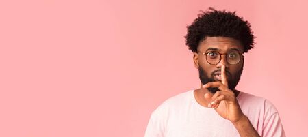 Quiet african guy in glasses showing hush gesture over pink background, panorama with free spaceの写真素材