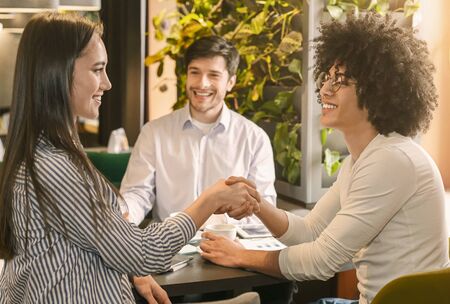 Agreement of investors. Happy man watching his partners handshaking during business lunch
