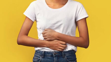 Symptoms Of Food Poisoning. Close-up of african girl holding hands on stomach suffering from...