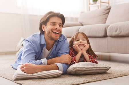 Happy family father and little daughter watching cartoons, lying on floor at home, free spaceの写真素材