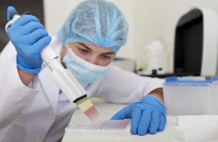 Woman preparing pink samples from pipette for analysing on high quality equipment, blurred backgroundの写真素材