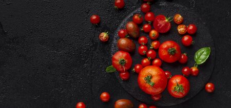 Tomato pasta recipe. Red big and small tomatoes decorating by basil leaf on black background, panorama, copy spaceの写真素材