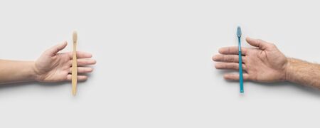 Save the planet concept. Two hands holding plastic and bamboo toothbrushes on white background, copy...