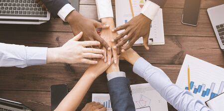Friendship and teamwork. Multiethnic coworkers stacking hands together in office, top view, panorama