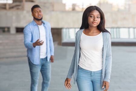 Couple breaking up after arguing outdoors, sad black woman leaving her complaining boyfriend that begging her to stayの写真素材
