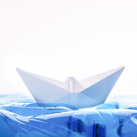 Plastic pollution conceptual. Paper boat on polluted ocean of bottles on white background, copy...