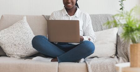 Online education. Unrecognizable black woman sitting on couch with laptop on lap, panorama