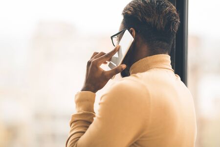 Back View. Portrait of african businessman talking on the phone at office, looking at window, copy spaceの写真素材