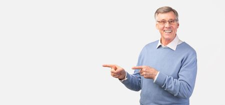 Look There. Cheerful Elderly Man Pointing Fingers Aside At Copy Space Standing Over White Studio Background. Panoramaの写真素材