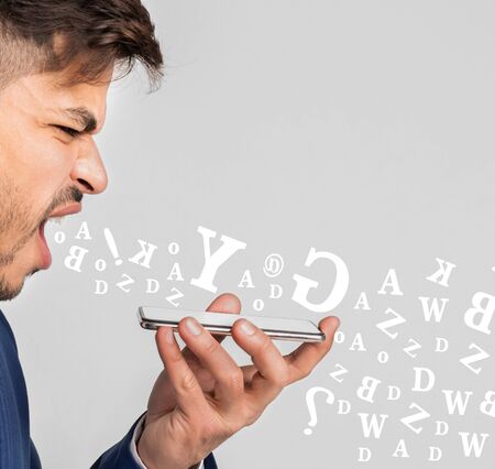 Angry businessman screaming at smartphone, having stressful conversation, diverse alphabet letters flying out of his mouth over light backgroundの写真素材