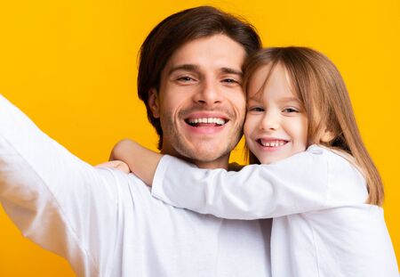 Portrait of happy father and little daughter taking selfie over yellow studio background, fatherhood conceptの写真素材