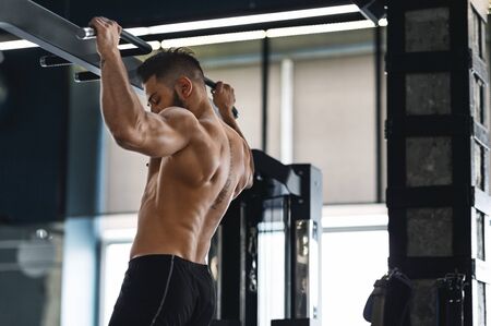 Muscular athlete pulling up on horizontal bar at gym, free space