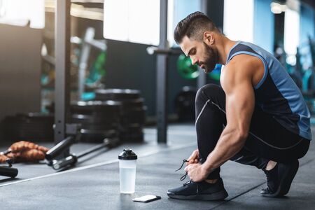 Fitness workout. Young athlete tying sneakers laces at gym, empty spaceの写真素材