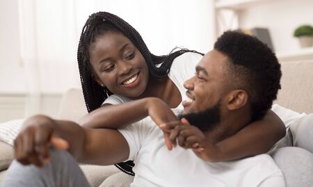 Romantic black couple relaxing at home, embracing and enjoying weekend together, resting in living room.の写真素材