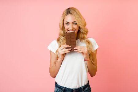 Sweet tooth concept. Young girl want to eat milk chocolate over pink backgroundの写真素材