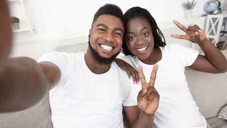 Joyful african american couple taking selfie and showing peace gesture, posing together at home, selective focus on people, panoramaの写真素材