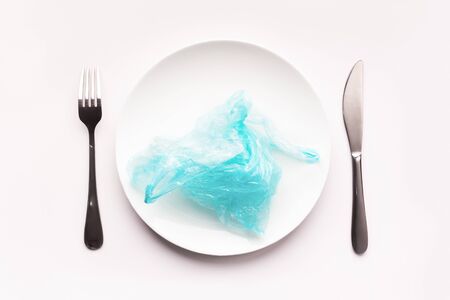 Eating plastic trash or consuming junk food concept. Plate with plastic bag instead of food isolated on white backgroundの写真素材