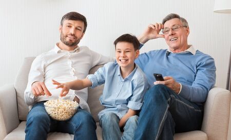 Grandfather, Father And Son Watching TV Switching Channels Sitting On Sofa At Home. Family Movies....