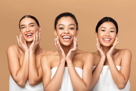 Skincare And Beauty. Three Multiracial Girls Touching Face With Perfect Smooth Skin On Cheeks Smiling At Camera Over Beige Backgroundの写真素材